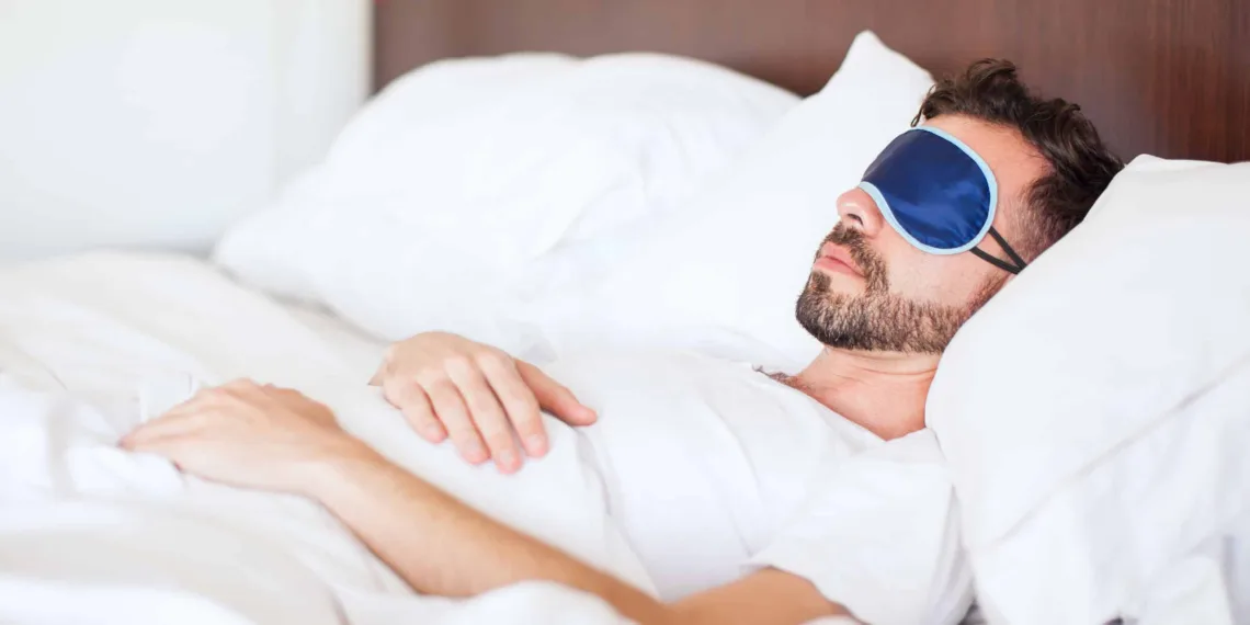 Portrait of a young man with a beard using a sleep mask to get some rest in a hotel