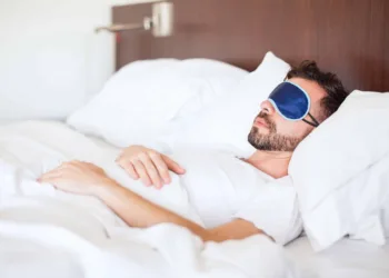 Portrait of a young man with a beard using a sleep mask to get some rest in a hotel