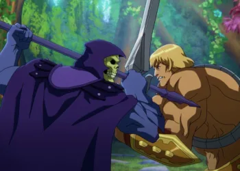 In a CG animated still from Masters of the Universe: Revelation, Skeletor (left), who wears a purple cloak and hood over his skull, grips his spear in a battle against He-Man (right), a strong shirtless blonde male with a golden armored belt and wrist plates holding a silver sword. The two are standing face to face in a forest with bright foliage.